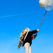Kind hebt einen langen Stab mit weißen und transparenten Ballons in den blauen Himmel.