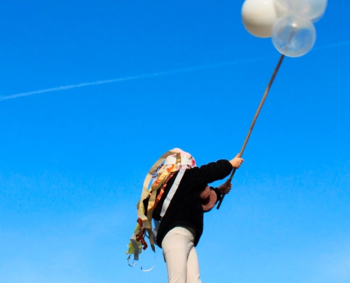 Kind hebt einen langen Stab mit weißen und transparenten Ballons in den blauen Himmel.