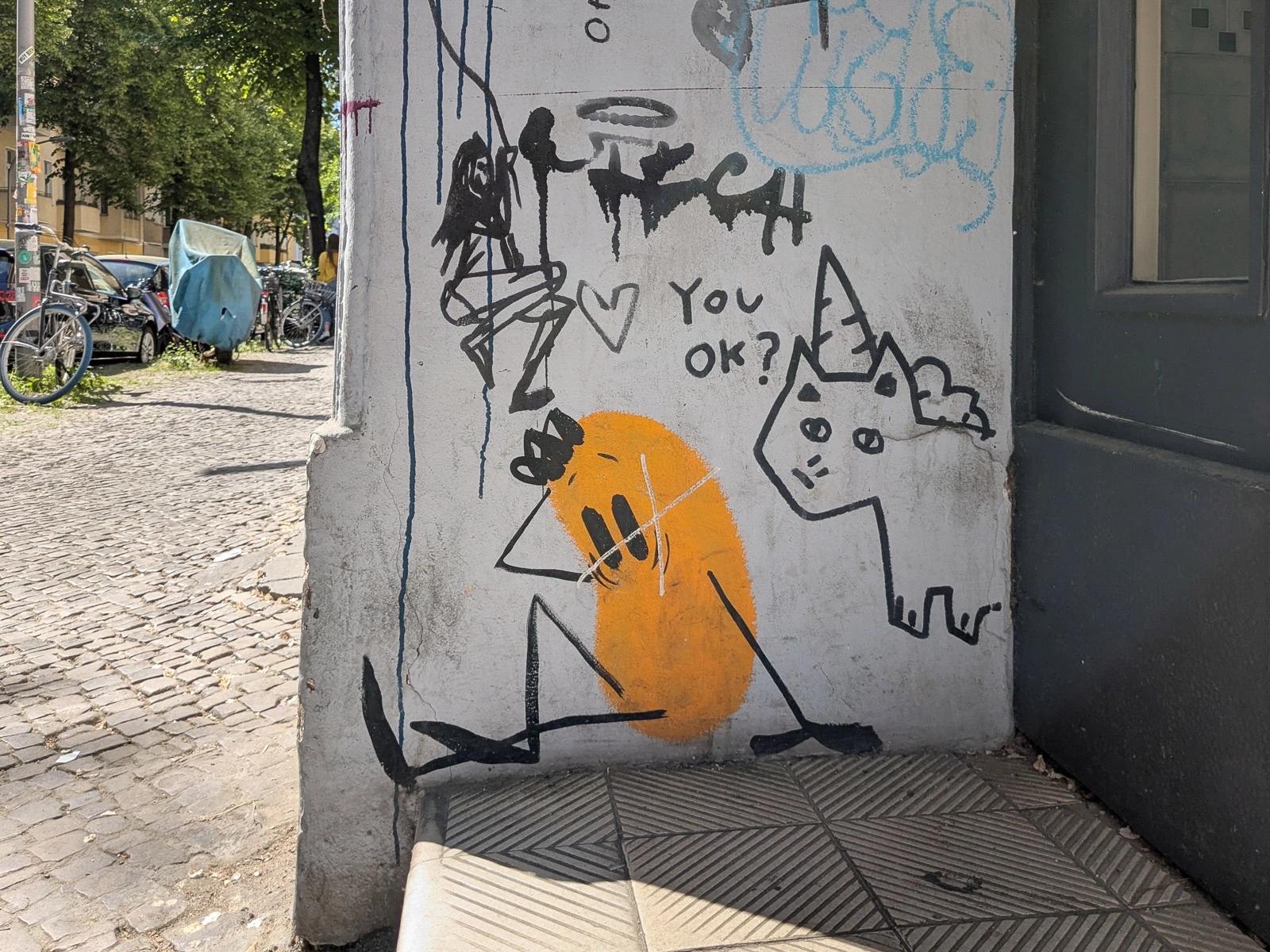 Graffiti an einer Hauswand in Neukölln mit „You ok?“, einer Katze und einem orangefarbenen Motiv.