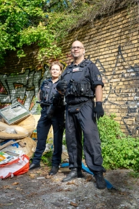 kms-sonne_Ordnungsamt-42 Zwei Mitarbeitende des Ordnungsamts stehen vor einer Graffitiwand neben abgestelltem Müll in Berlin-Neukölln.